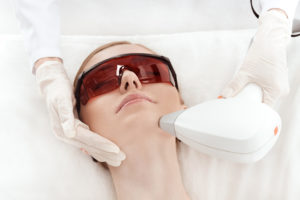 Close-up view of young woman in uv protective glasses receiving laser skin care on face